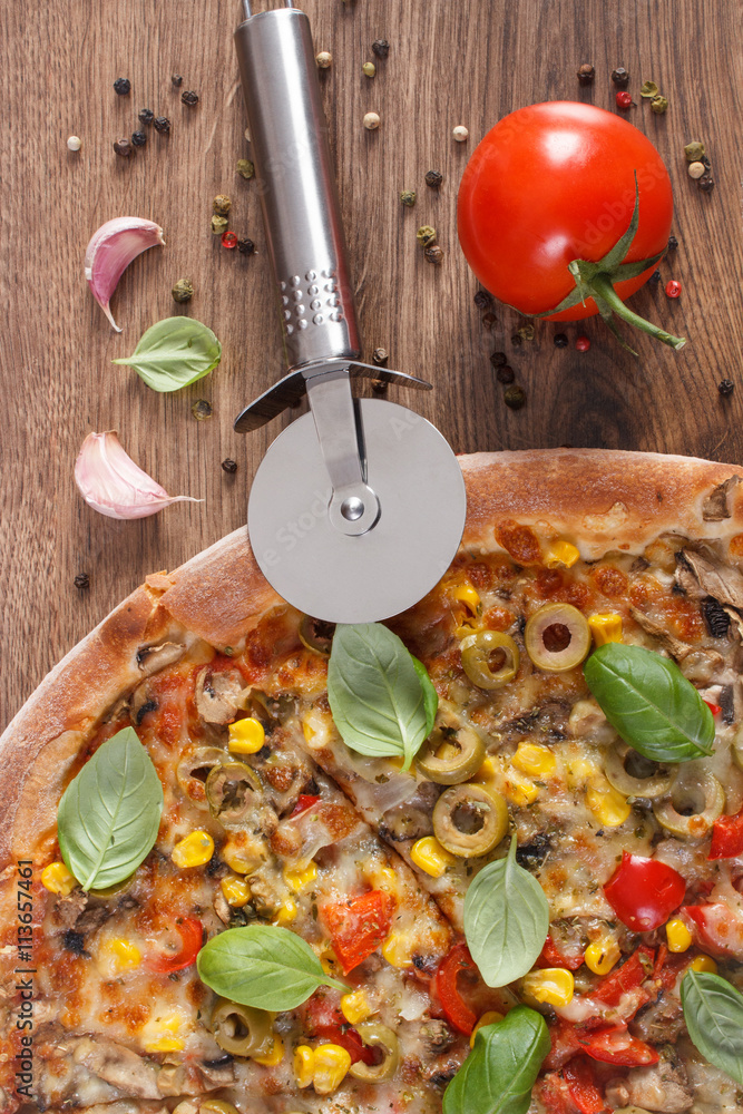 Pizza cutter with vegetarian pizza, ingredients with spices on wooden background, fast food