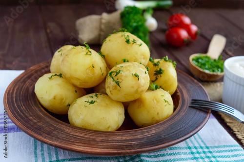 Young boiled potatoes with butter and dill in a clay bowl on a wooden background. Close up
