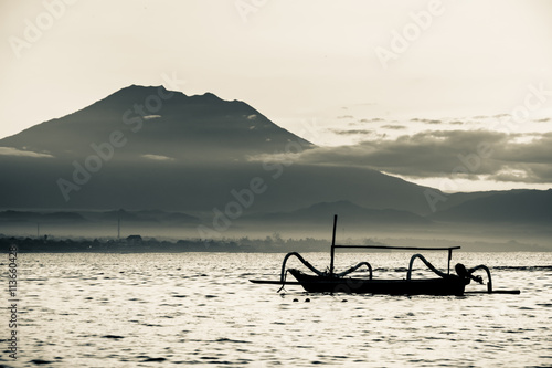 Indonesian outrigger canoe with scenic background of Mount Agung peak above the clouds on a clear day.