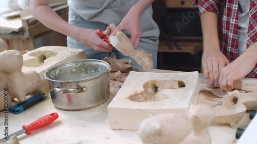 Tilt up of two young female artists making papier mache dog figures of craft paper together at small handmade studio, shaky camera shot on Sony NEX 700 + Odyssey 7Q photo