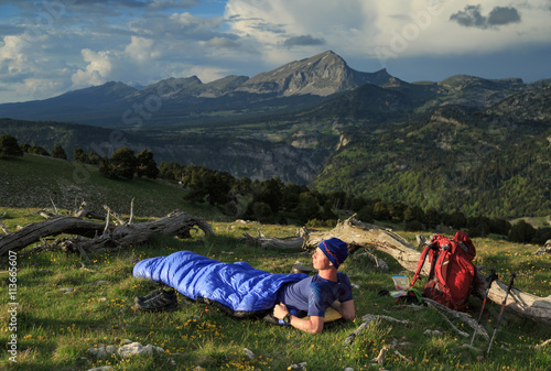 Hiker preparing for a bivaque in his sleepingbag between two dead trees in the hills.