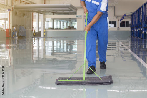 worker in blue, protective uniform cleaning new epoxy floor in e