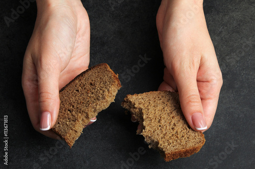 girl breaks a piece of bread on black background.The concept of poverty