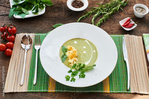 Top view of soup with zucchini in a white plate on a wooden table