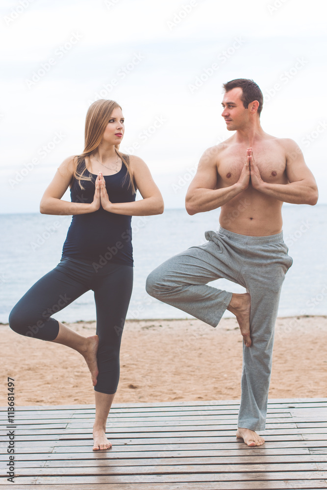 Man and pregnant girl are doing yoga on the beach