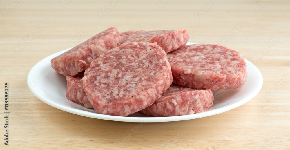 Sausage patties on a white plate atop a wood table side view.