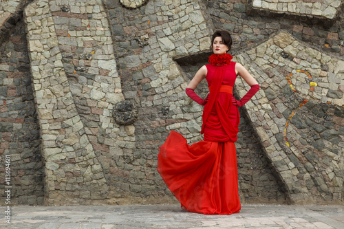 Portrait of beautiful woman in red dress on stone wall background decoration © Diana Savich