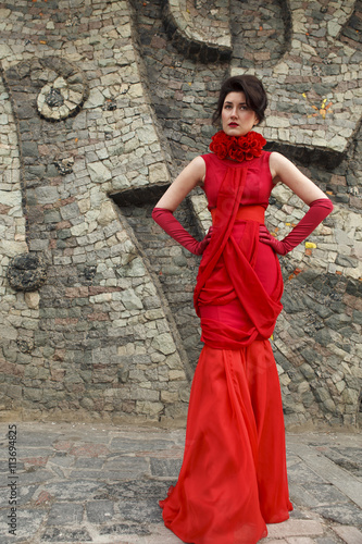 Portrait of beautiful woman in red dress on stone wall background decoration