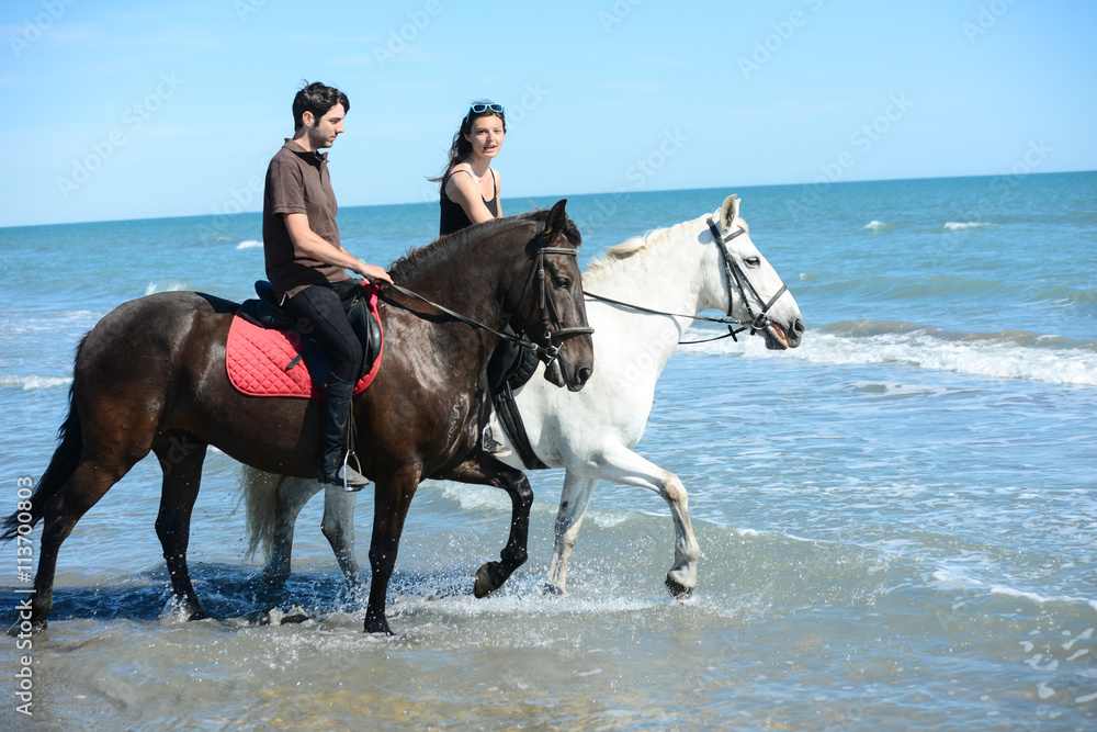 happy young couple vacation riding horses on the beach in sunny summer day happy young couple vacation riding horses on the beach in sunny summer day