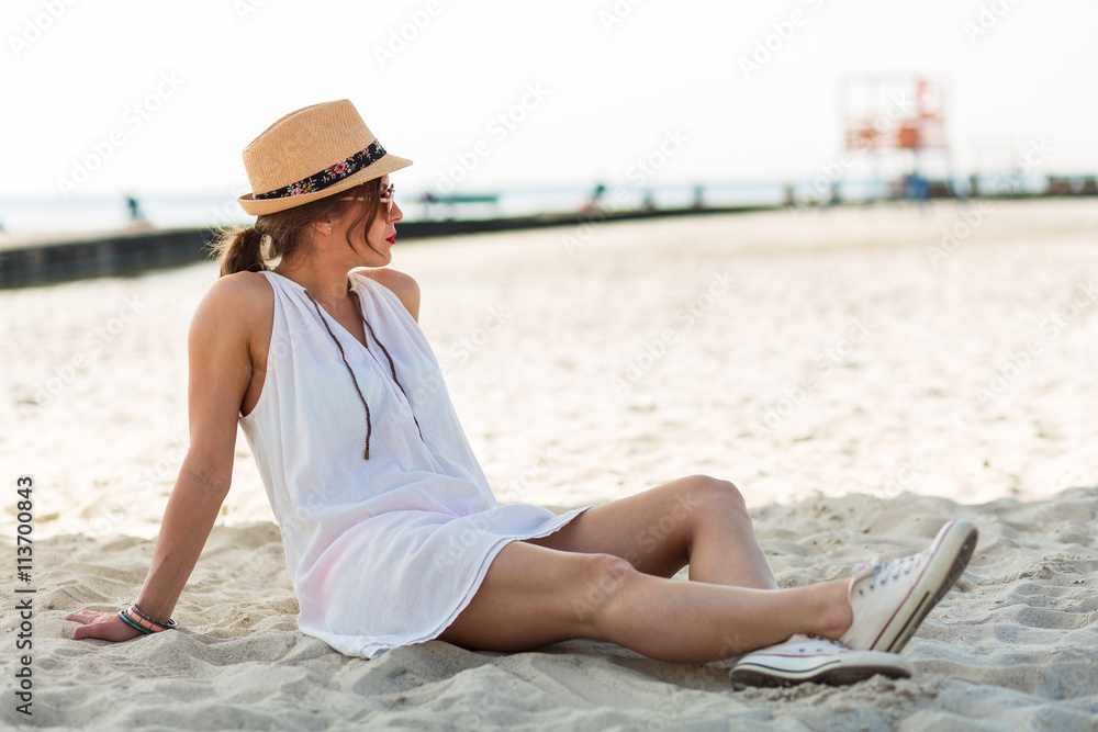 Stylish woman sitting on a sandy beach at summer