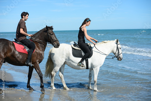 happy young couple vacation riding horses on the beach in sunny summer day