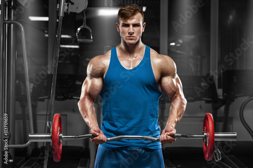Muscular man working out in gym doing exercises with barbell at biceps, strong male