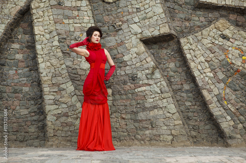 Portrait of beautiful woman in red dress on stone wall background decoration © Diana Savich