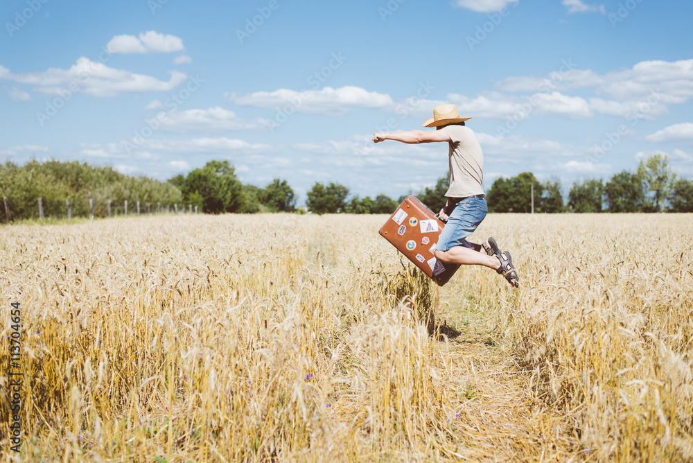 Man in hat jumping with old suitcase on wheat field summer sunny countryside. Man in hat jumping with old suitcase on wheat field summer sunny countryside.
