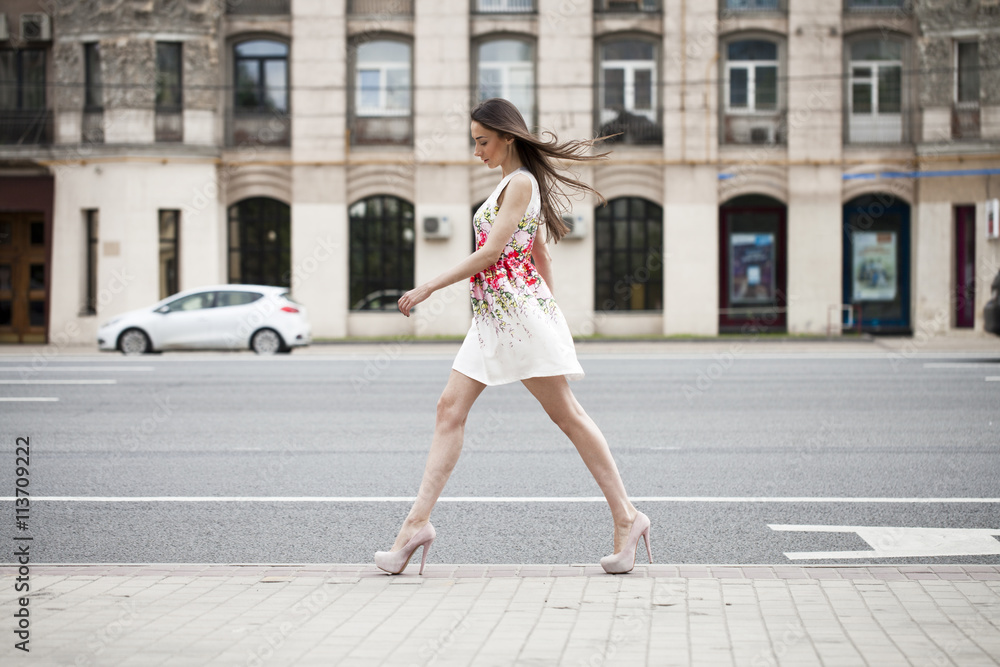 Young beautiful brunette woman in white flowers dress walking on