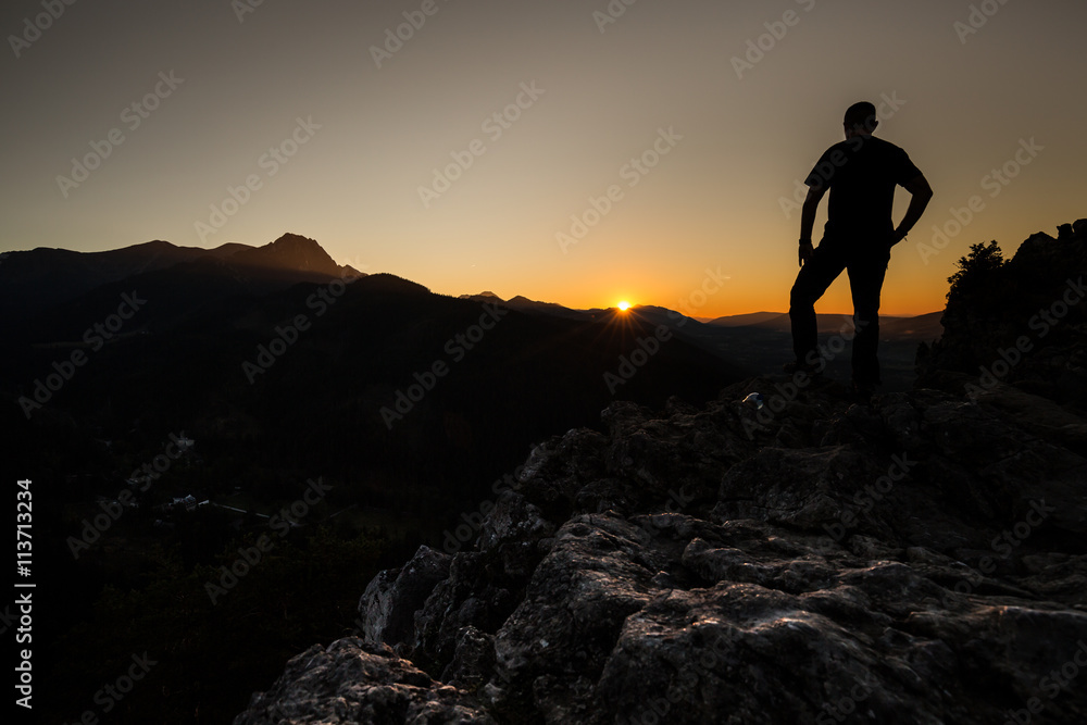 Hiker on a mountain top at sunset. Men admiring mountain lands
