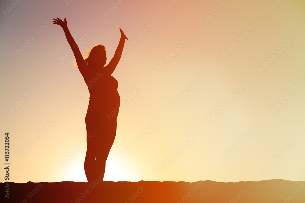 Silhouette of happy pregnant woman at sunset