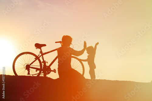 Silhouette of father and little daughter biking at sunset