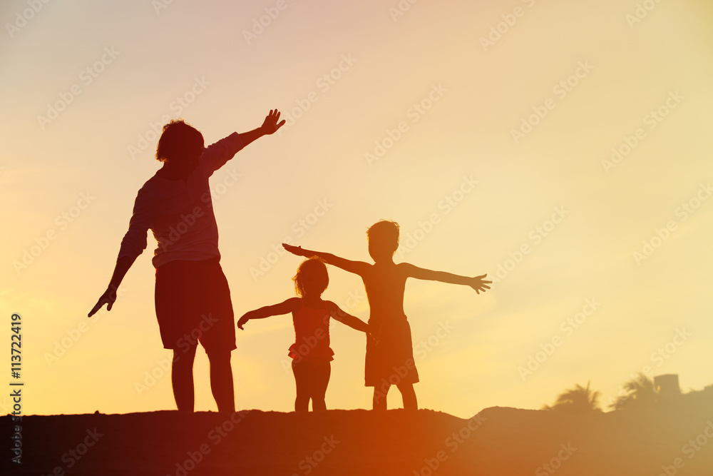 father with son and daughter silhouettes play at sunset