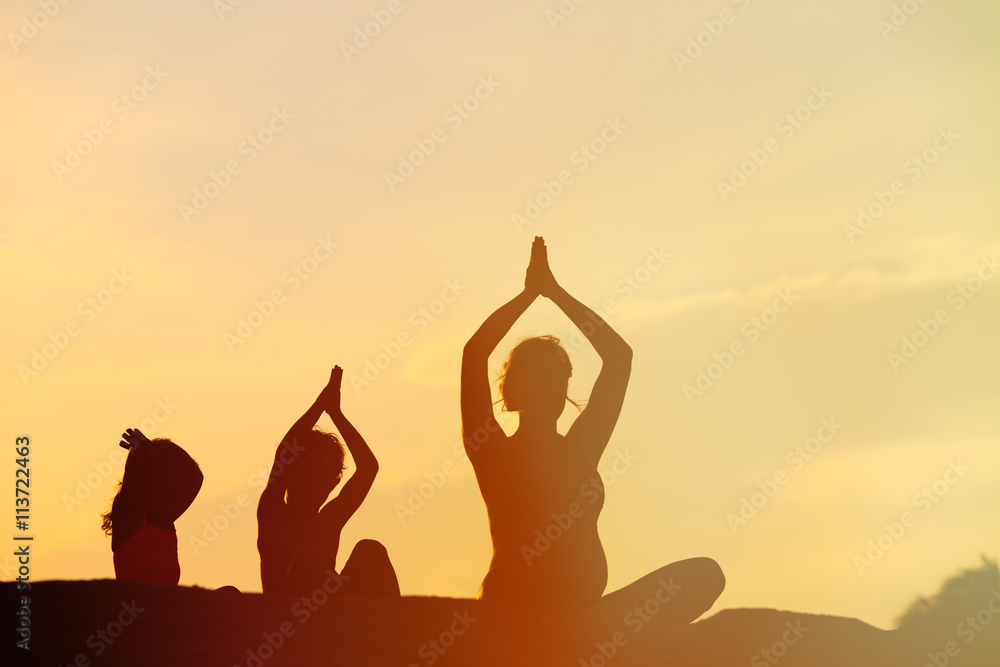 silhouette of mother and kids doing yoga at sunset