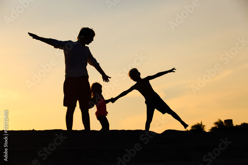 father with son and daughter silhouettes play at sunset