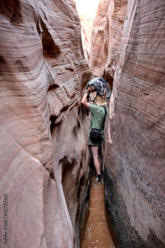 Man hiker squeezing through Zebra slot canyon, Escalante National Monument, Utah, USA. 