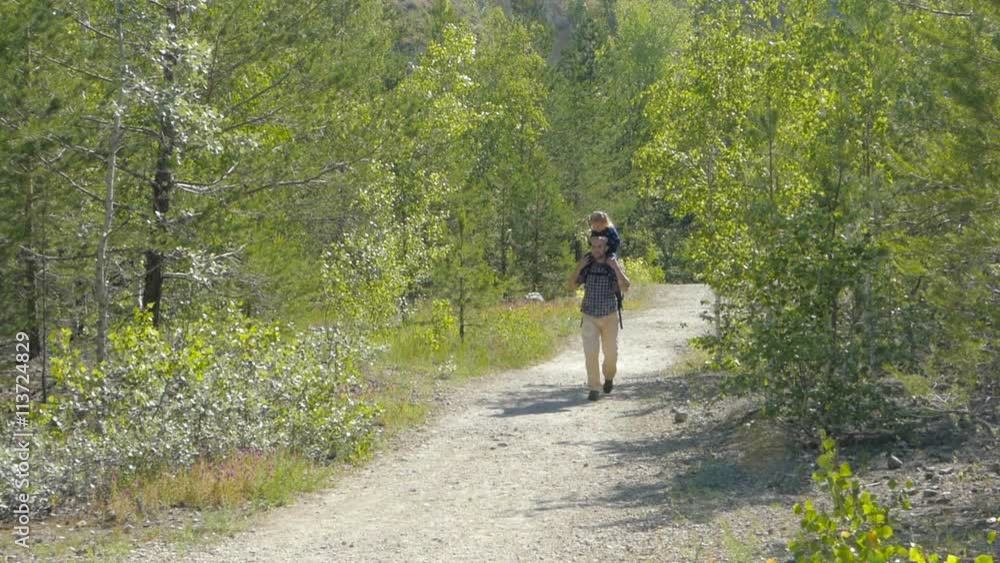 Daughter sits on the shoulders of his father walking outdoors on a forest path. Daughter sits on the shoulders of his father walking outdoors on a forest path.