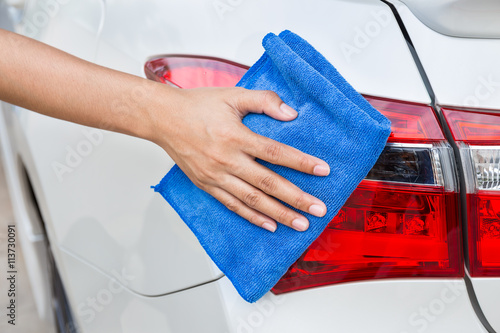 Hand with blue microfiber cloth cleaning taillight white car. © powerbeephoto