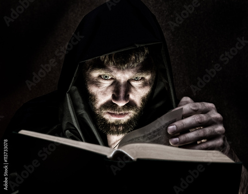 necromancer casts spells from thick ancient book by candlelight on a dark background