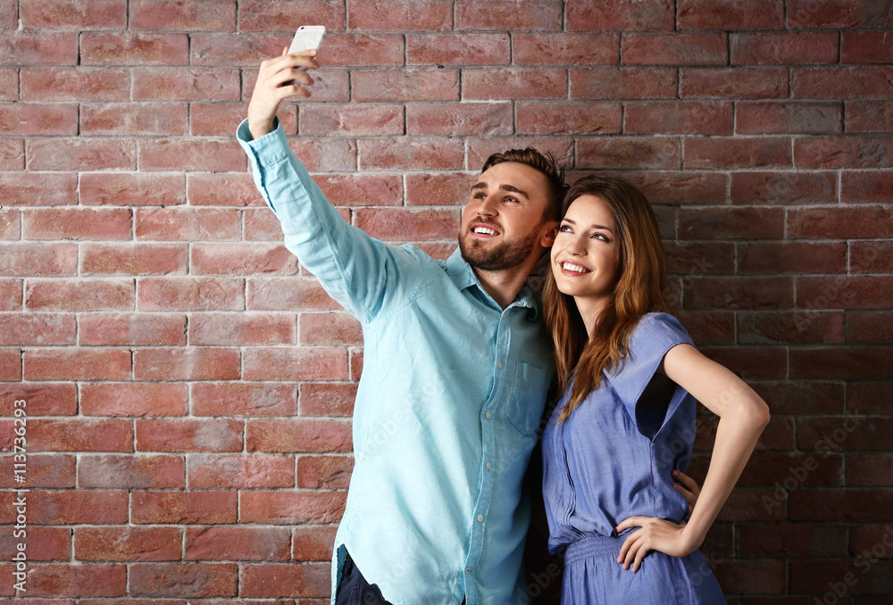 Young cheerful friends taking selfie on brick wall background Young cheerful friends taking selfie on brick wall background