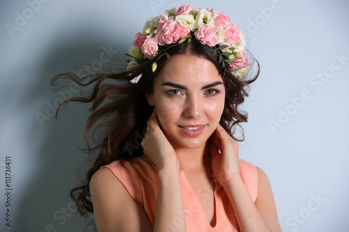 Beautiful young woman with flowers on head on light background