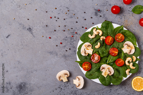 Salad with spinach, mushrooms and tomatoes on concrete backgroun