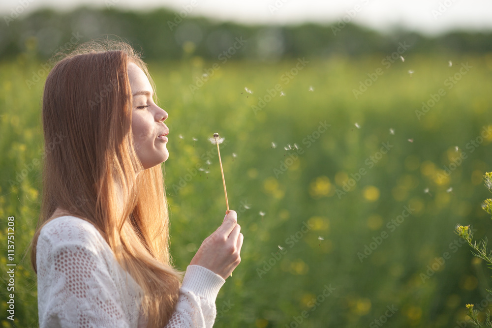 Young spring fashion woman blowing dandelion in spring garden. Springtime. Trendy girl at sunset in spring landscape background. Allergic to pollen of flowers. Spring allergy Young spring fashion woman blowing dandelion in spring garden. Springtime. Trendy girl at sunset in spring landscape background. Allergic to pollen of flowers. Spring allergy