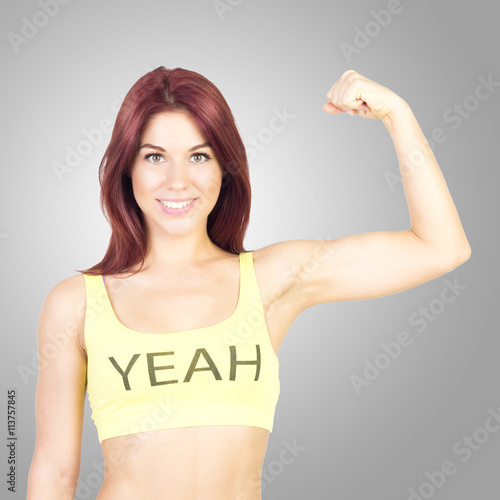Sport smiling woman shows off his muscles on gray background. Sports and fitness