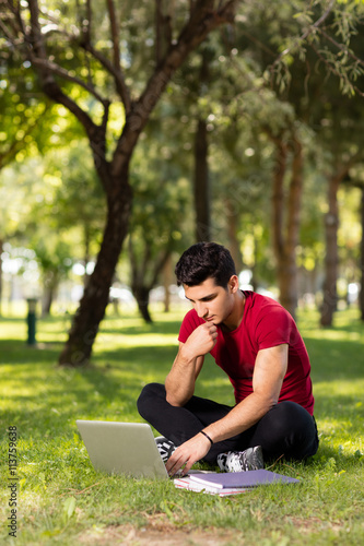 Teenage student working with laptop in park.