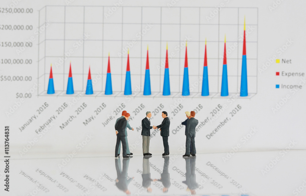 Selective focus of miniature businessman handshake with business chart background as commitment, partnership concept. Selective focus of miniature businessman handshake with business chart background as commitment, partnership concept.