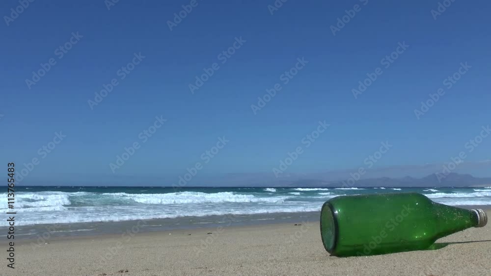 Empty green glass bottle lying on a sandy beach in front of the Atlantic ocean with waves rolling in, littering the beautiful, clean beach. Empty green glass bottle lying on a sandy beach in front of the Atlantic ocean with waves rolling in, littering the beautiful, clean beach.