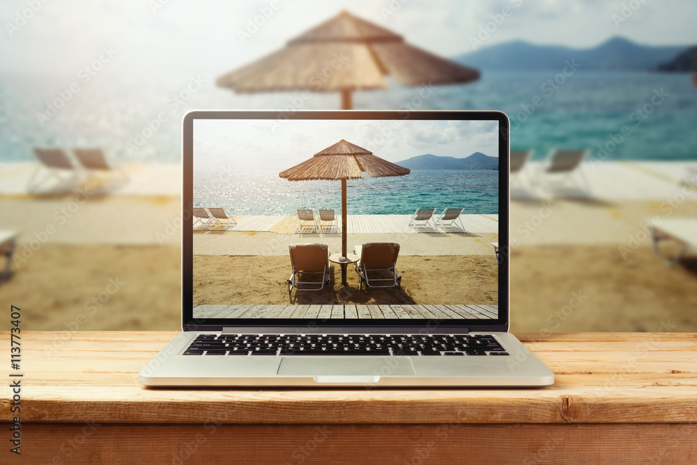 Laptop computer with sunny beach image on wooden table. Summer vacation photo sharing