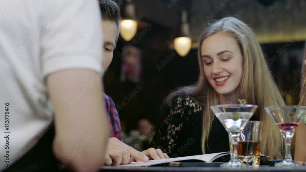 Happy young people sitting in the bar reading menu card Happy young people sitting in the bar reading menu card