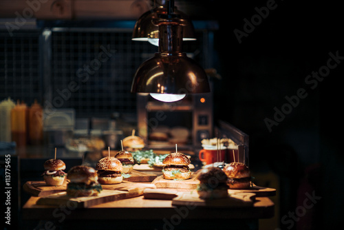 Gourmet Tasty Beef Burgers with Salad Slices on a Wooden Tray inside a bar waiting to be served