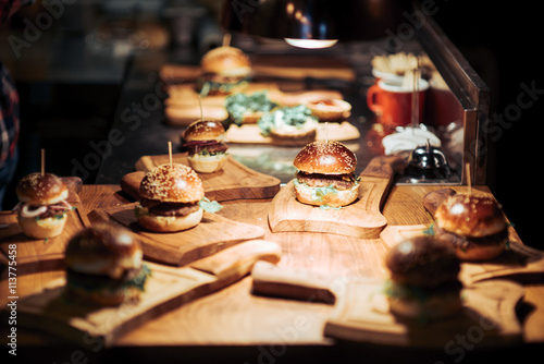 Gourmet Tasty Beef Burgers with Salad Slices on a Wooden Tray inside a bar waiting to be served