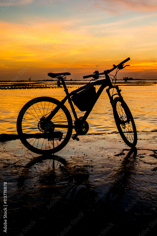 Fototapeta premium Silhouette of bicycle at jetty with sunset sky and sea backgroun