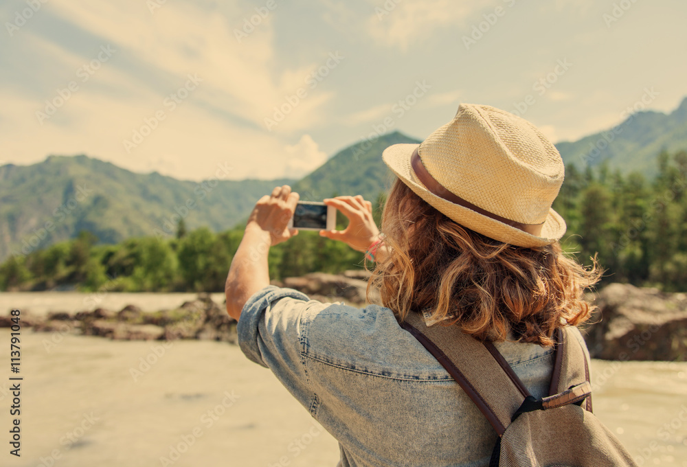 Young woman traveler on a background of mountains takes photos o