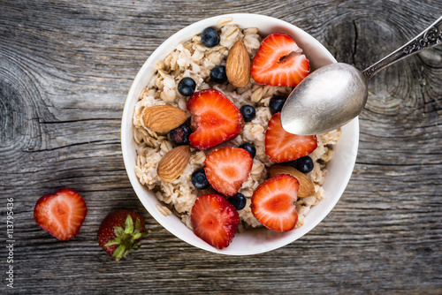 Oatmeal with almonds and berries in a bowl on wooden background. Top view. Diet breakfast.