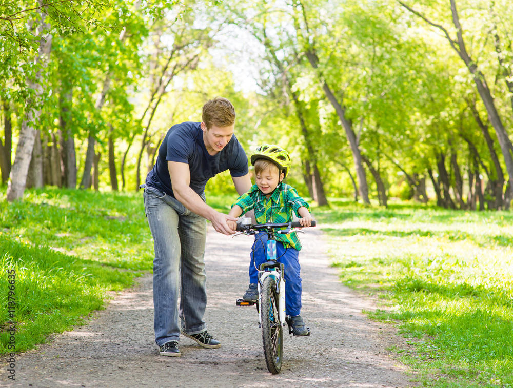 father teaches his son to ride a bike in park father teaches his son to ride a bike in park