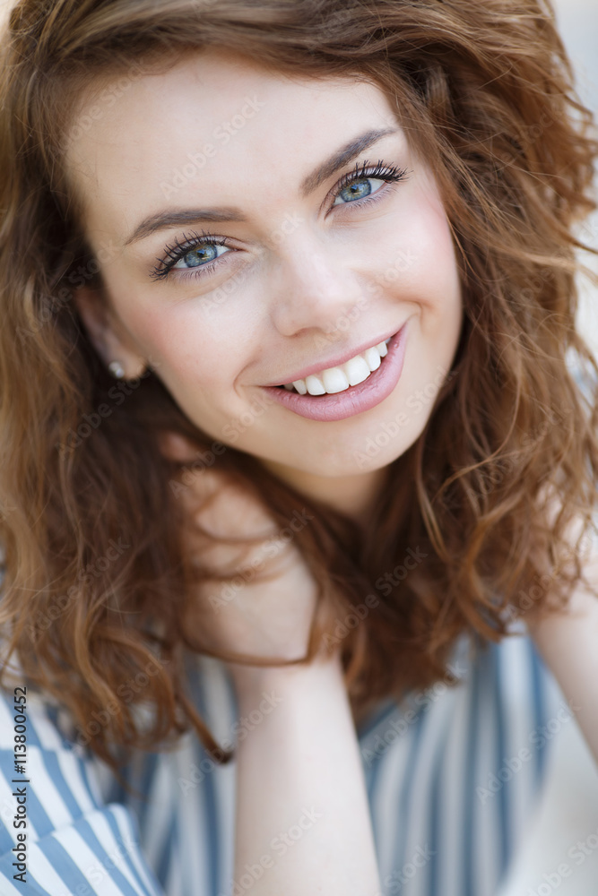 Beautiful girl with grey eyes and long curly red hair,a beautiful smile and straight white teeth,wearing earrings,wearing a light striped shirt,posing for a photographer in the summer outdoors Beautiful girl with grey eyes and long curly red hair,a beautiful smile and straight white teeth,wearing earrings,wearing a light striped shirt,posing for a photographer in the summer outdoors