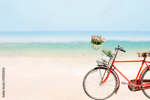 Old red Bicycle with basket flowers on blured beach tropical sea
