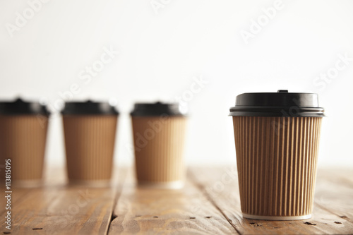 One focused craft paper coffee cup with black cap isolated on side in front of unfocused others on rustic aged wooden table photo