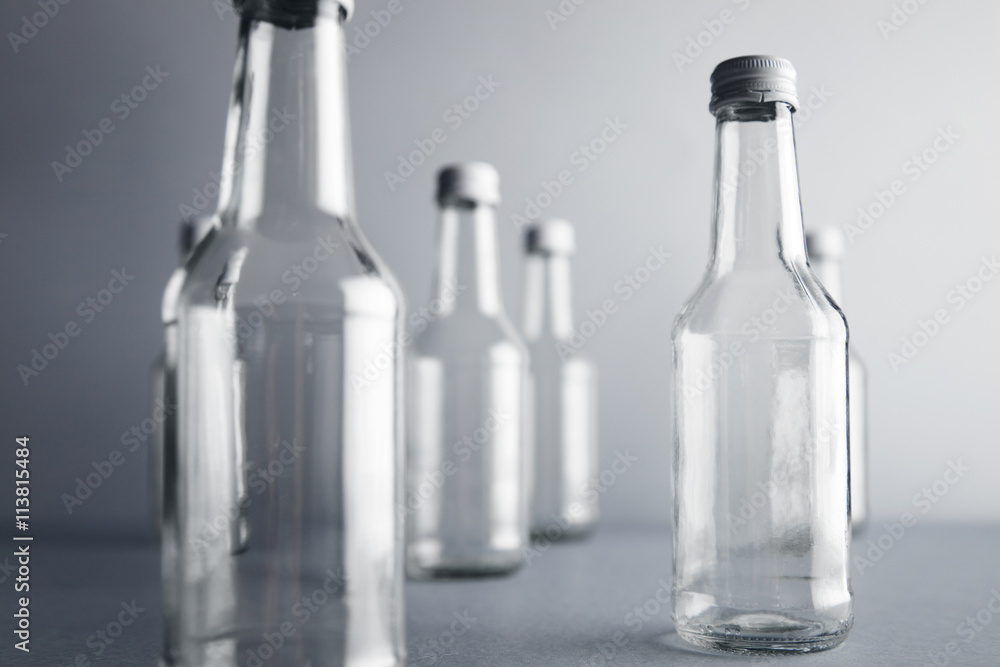 Close view on clear unlabeled empty glass bottles for cold beverages and drinks, randomly presented and isolated on gray background Close view on clear unlabeled empty glass bottles for cold beverages and drinks, randomly presented and isolated on gray background