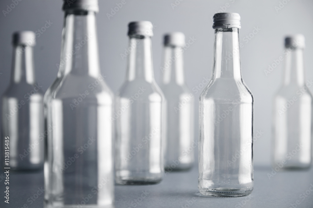 One focused empty clear transparent glass bottle for wine presented on right side and many unfocused bottles near, isolated on gray One focused empty clear transparent glass bottle for wine presented on right side and many unfocused bottles near, isolated on gray